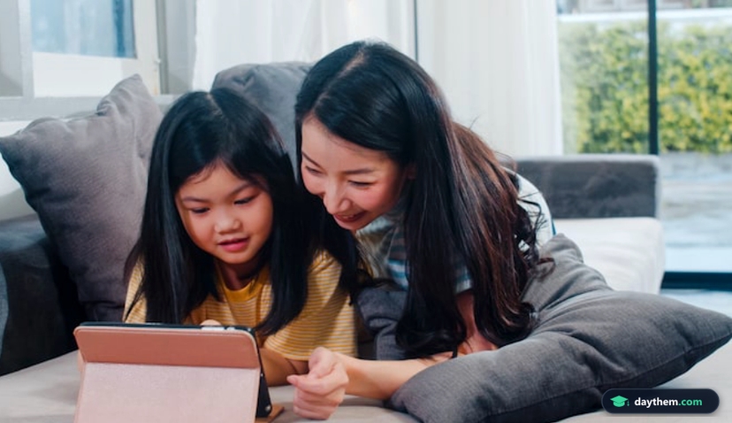 Young Asian family and daughter happy using tablet at home. Japanese mother relax with little girl watching movie lying on sofa in living room at house. Funny mom and lovely child are having fun.