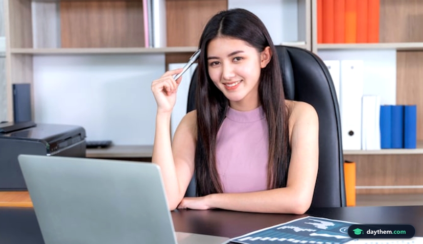 Nhân viên nữ trẻ châu Á chăm chú làm việc với laptop và tài liệu trên bàn làm việc tại văn phòng để xem lại hồ sơ hiệu suất sau một năm.